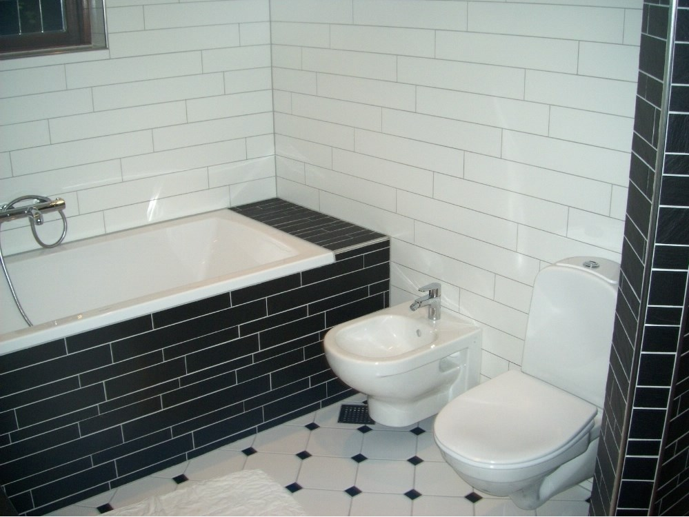 Et smukt nyt badeværelse med badekar og fliser i hvid med sorte fliser omkring badekaret. 